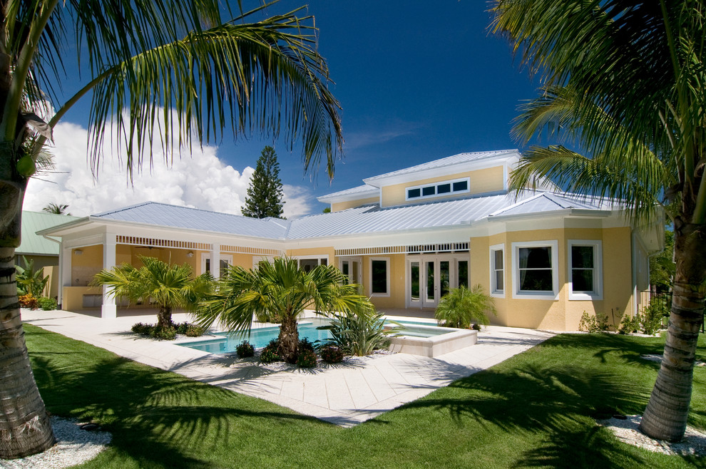 This is an example of a mid-sized tropical two-storey stucco yellow house exterior in Miami with a hip roof and a metal roof.