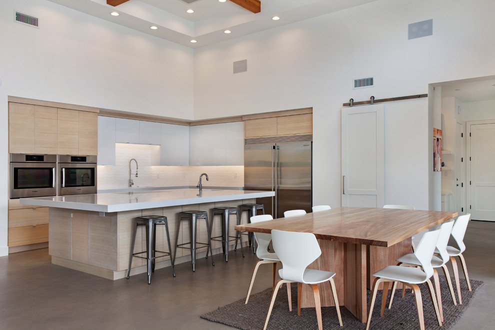 Large contemporary l-shaped open plan kitchen in Orange County with an undermount sink, flat-panel cabinets, light wood cabinets, quartzite benchtops, white splashback, subway tile splashback, stainless steel appliances, concrete floors and with island.