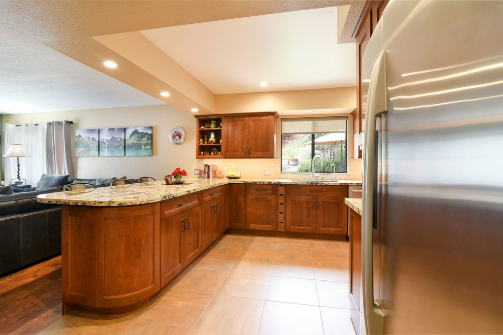 This is an example of a large galley eat-in kitchen in Other with an undermount sink, recessed-panel cabinets, medium wood cabinets, granite benchtops, white splashback, subway tile splashback, stainless steel appliances, porcelain floors, a peninsula and beige floor.