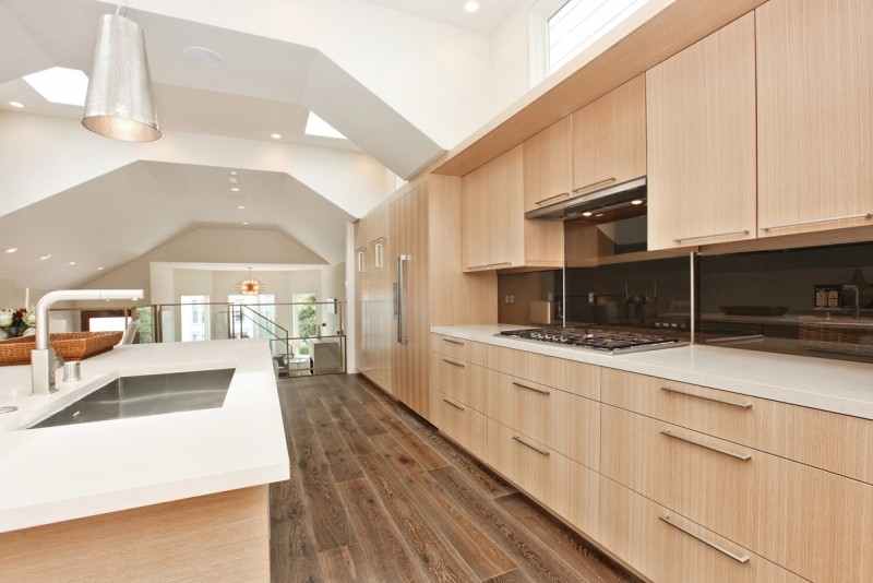 Photo of a mid-sized contemporary u-shaped eat-in kitchen in San Francisco with an undermount sink, flat-panel cabinets, light wood cabinets, quartz benchtops, black splashback, stone slab splashback, panelled appliances, porcelain floors, with island, brown floor and white benchtop.