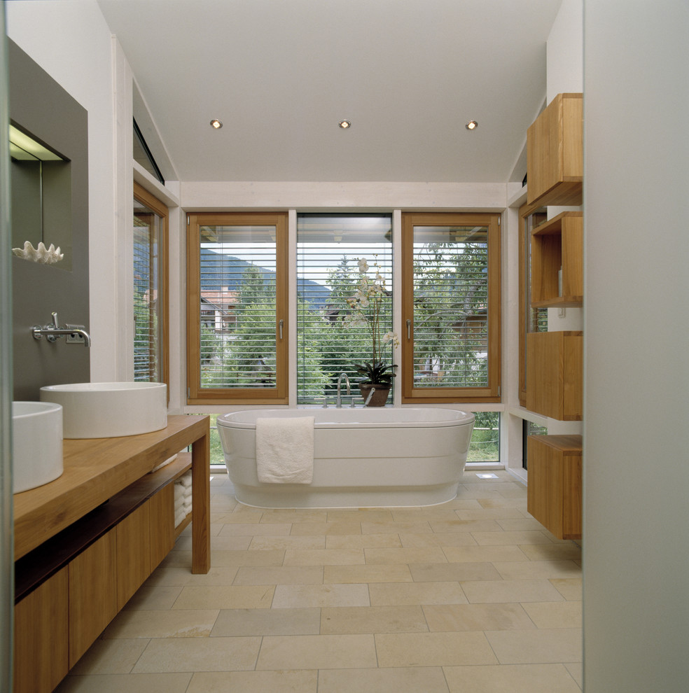 This is an example of a large contemporary bathroom in Other with open cabinets, medium wood cabinets, a freestanding tub, white walls, limestone floors, a vessel sink and wood benchtops.