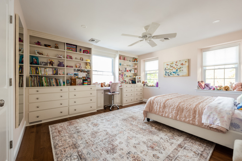 This is an example of a transitional kids' bedroom for girls in Philadelphia with pink walls and dark hardwood floors.