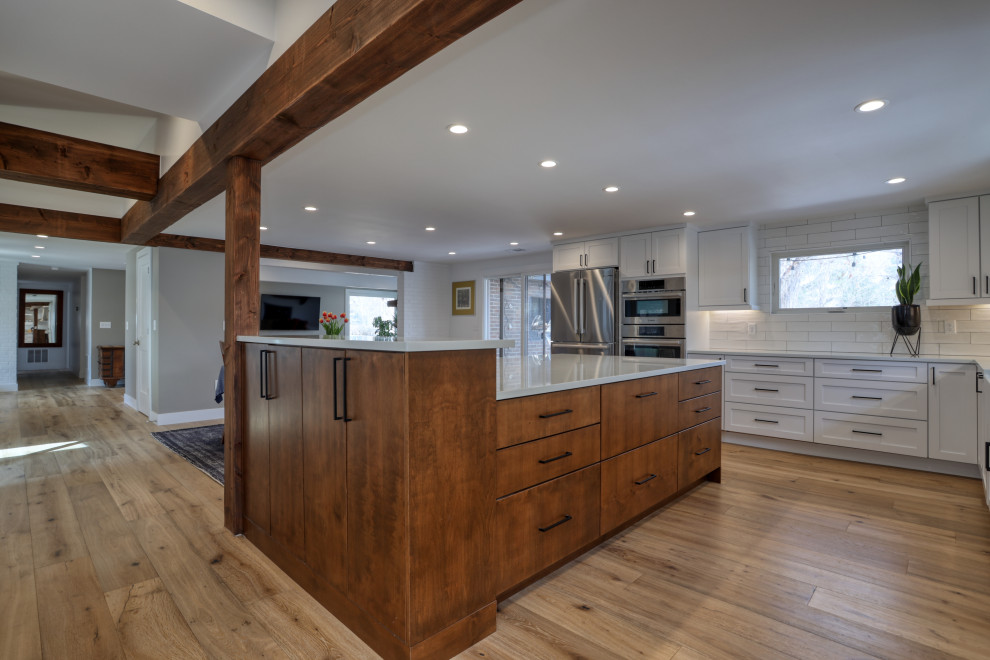 Inspiration for a large transitional l-shaped light wood floor and brown floor kitchen remodel with a farmhouse sink, recessed-panel cabinets, white cabinets, quartz countertops, white backsplash, stainless steel appliances, an island and white countertops