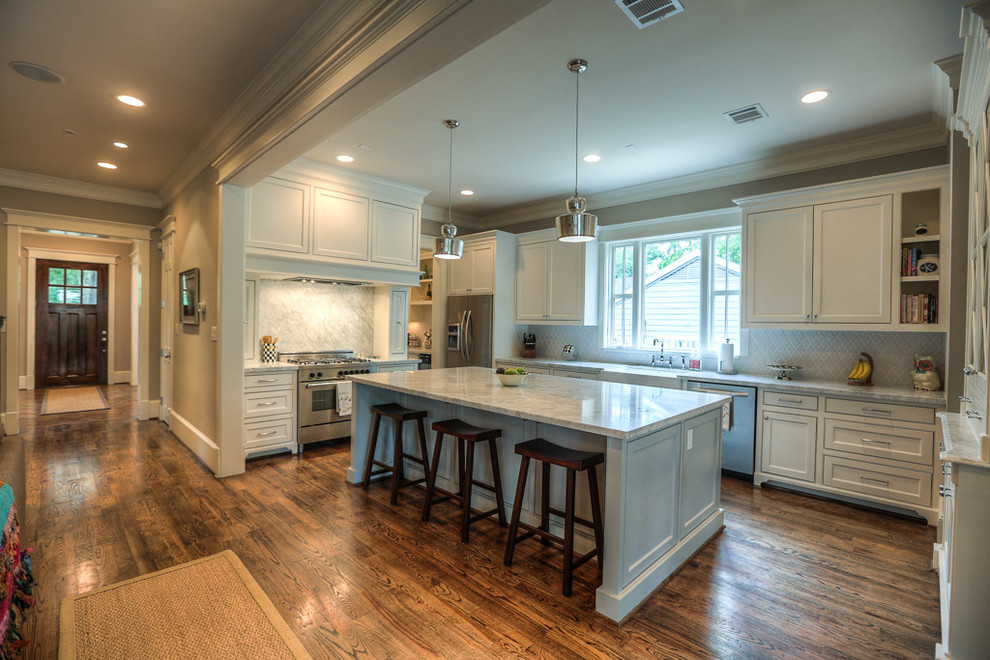 This is an example of a large arts and crafts u-shaped kitchen in Houston with a farmhouse sink, shaker cabinets, white cabinets, marble benchtops, grey splashback, ceramic splashback, stainless steel appliances, medium hardwood floors and with island.