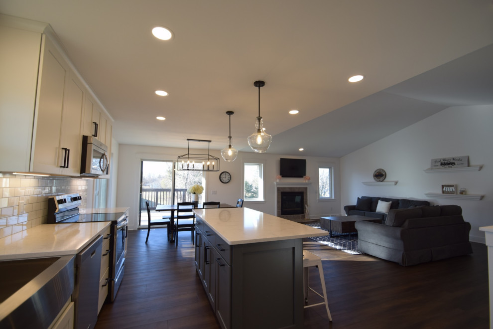 Mid-sized transitional single-wall vinyl floor open concept kitchen photo with a farmhouse sink, shaker cabinets, quartz countertops, white backsplash, subway tile backsplash, stainless steel appliances, an island and white countertops