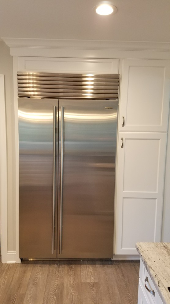Mid-sized transitional u-shaped medium tone wood floor and brown floor eat-in kitchen photo in Philadelphia with an undermount sink, recessed-panel cabinets, white cabinets, granite countertops, gray backsplash, glass tile backsplash, stainless steel appliances and a peninsula
