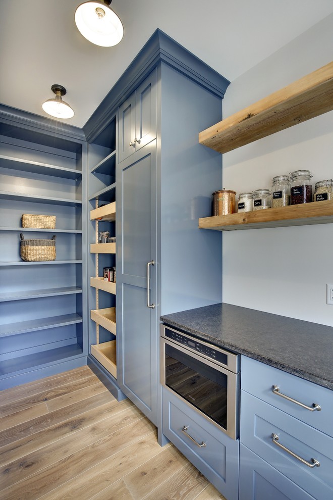 Design ideas for a mid-sized country l-shaped kitchen pantry in Minneapolis with a farmhouse sink, shaker cabinets, blue cabinets, quartzite benchtops, black splashback, subway tile splashback, panelled appliances, light hardwood floors and with island.