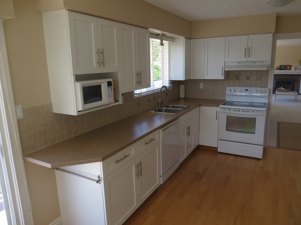 This is an example of a mid-sized contemporary u-shaped separate kitchen in Vancouver with a drop-in sink, shaker cabinets, white cabinets, laminate benchtops, beige splashback, ceramic splashback, white appliances, light hardwood floors and no island.
