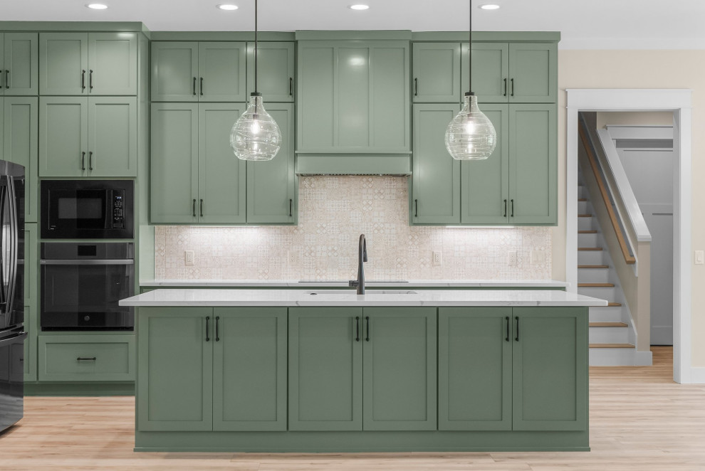 Example of an arts and crafts l-shaped vinyl floor and beige floor open concept kitchen design with an undermount sink, shaker cabinets, green cabinets, quartzite countertops, beige backsplash, porcelain backsplash, stainless steel appliances, an island and white countertops