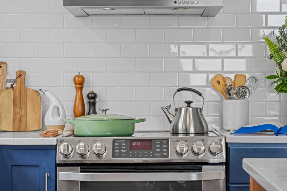Foto på ett vintage vit l-kök, med en rustik diskho, skåp i shakerstil, blå skåp, vitt stänkskydd, stänkskydd i keramik, rostfria vitvaror, mellanmörkt trägolv och en köksö