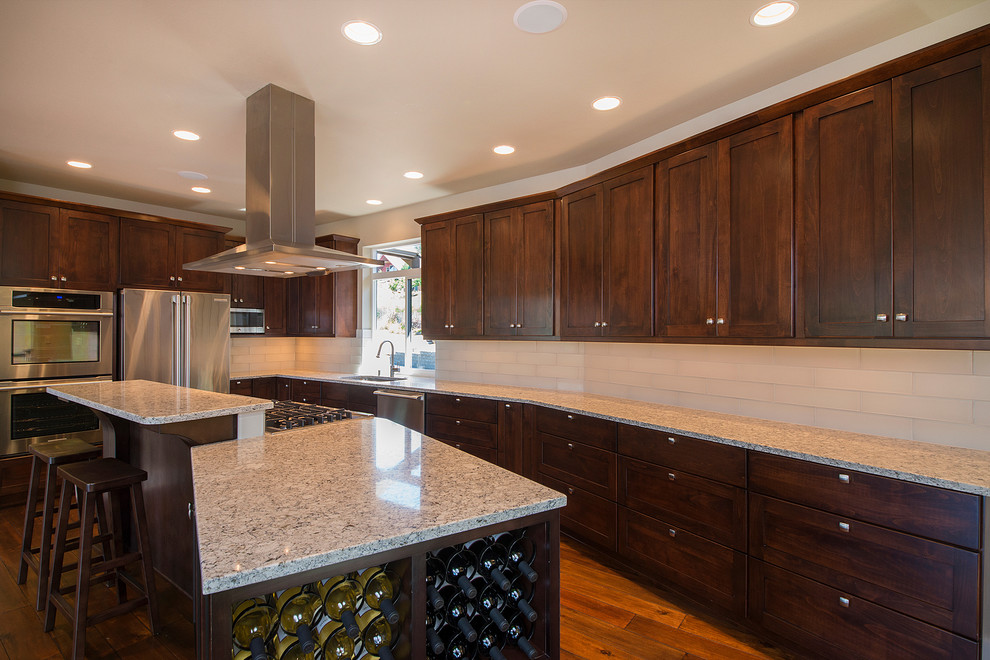 Inspiration for a large transitional l-shaped medium tone wood floor eat-in kitchen remodel in Seattle with a drop-in sink, shaker cabinets, dark wood cabinets, granite countertops, white backsplash, glass tile backsplash, stainless steel appliances and two islands