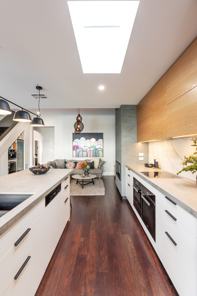 Photo of a mid-sized galley kitchen pantry in Adelaide with a double-bowl sink, black cabinets, concrete benchtops, white splashback, stone slab splashback, black appliances, dark hardwood floors, with island, brown floor and grey benchtop.