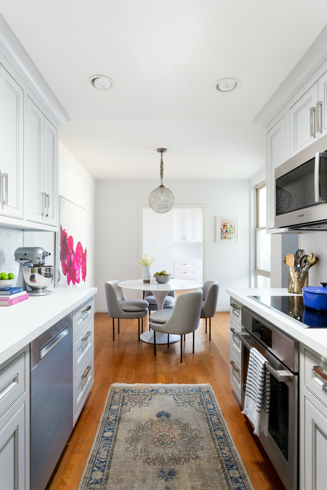 Inspiration for a mid-sized transitional galley eat-in kitchen in Los Angeles with beaded inset cabinets, white cabinets, stainless steel appliances, medium hardwood floors, no island, brown floor, white benchtop, an undermount sink, quartz benchtops, white splashback and porcelain splashback.