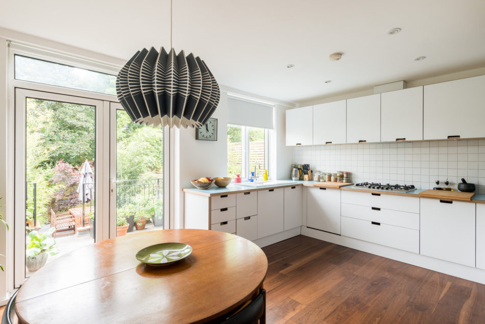 Mid-sized midcentury u-shaped eat-in kitchen in Other with a double-bowl sink, flat-panel cabinets, white cabinets, wood benchtops, white splashback, cement tile splashback, stainless steel appliances, medium hardwood floors, no island, brown floor and blue benchtop.