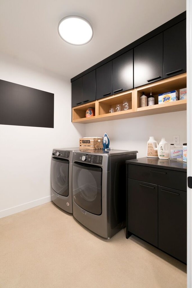 Large modern single-wall dedicated laundry room in Other with flat-panel cabinets, black cabinets, white walls, concrete floors, a side-by-side washer and dryer and grey floor.