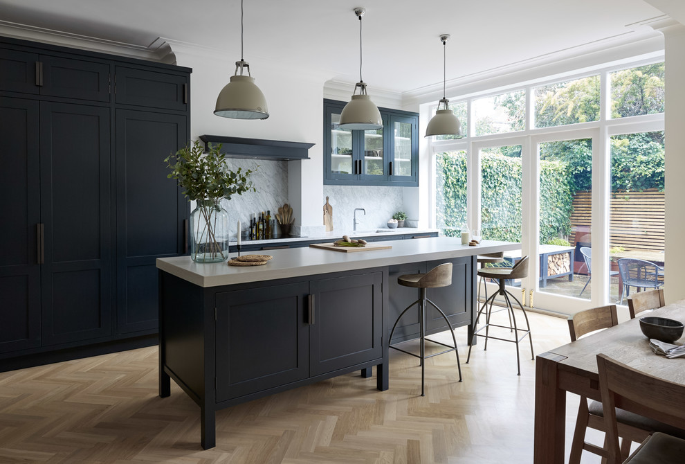 Design ideas for a large country galley eat-in kitchen in London with an integrated sink, shaker cabinets, blue cabinets, concrete benchtops, white splashback, marble splashback, panelled appliances, light hardwood floors, with island, beige floor and white benchtop.