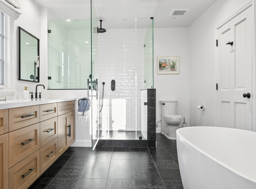This is an example of a large transitional master bathroom in Los Angeles with shaker cabinets, a freestanding tub, white tile, subway tile, white walls, porcelain floors, engineered quartz benchtops, black floor, white benchtops, light wood cabinets, a corner shower, a two-piece toilet and a hinged shower door.