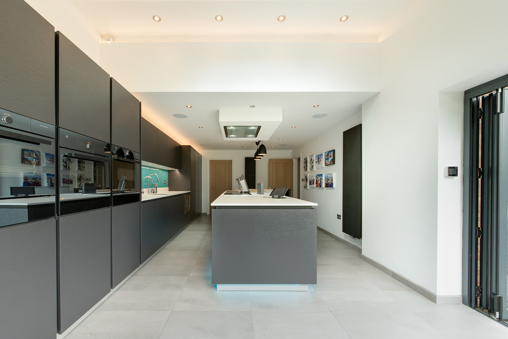 This is an example of a large contemporary single-wall eat-in kitchen in Buckinghamshire with an undermount sink, flat-panel cabinets, black cabinets, quartz benchtops, blue splashback, glass sheet splashback, panelled appliances, ceramic floors, with island and grey floor.