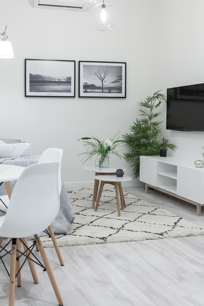 This is an example of a small scandinavian open concept family room in Madrid with white walls, laminate floors, no fireplace, a wall-mounted tv and grey floor.