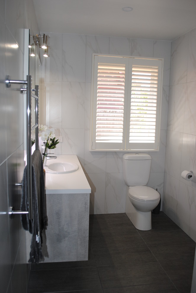 This is an example of a mid-sized contemporary master bathroom in Other with furniture-like cabinets, grey cabinets, an open shower, a two-piece toilet, white tile, ceramic tile, white walls, porcelain floors, a drop-in sink, laminate benchtops, grey floor and an open shower.