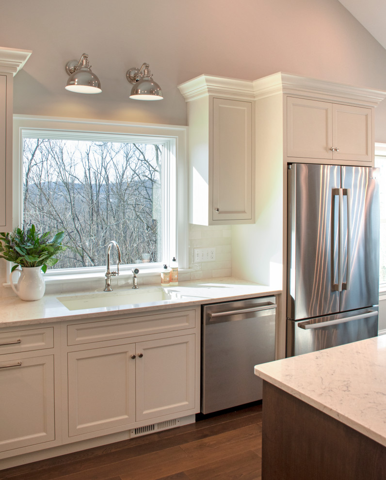 Transitional medium tone wood floor, white floor and vaulted ceiling eat-in kitchen photo with an undermount sink, shaker cabinets, white cabinets, quartz countertops, white backsplash, ceramic backsplash, stainless steel appliances, an island and white countertops