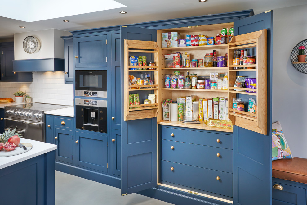This is an example of a large traditional l-shaped eat-in kitchen in Other with shaker cabinets, blue cabinets, quartzite benchtops, white splashback, subway tile splashback, stainless steel appliances, concrete floors, with island, grey floor and white benchtop.