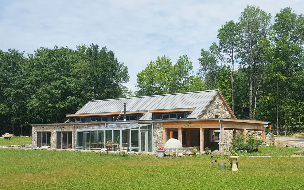 This is an example of a country house exterior in New York with stone veneer, a gable roof and a metal roof.