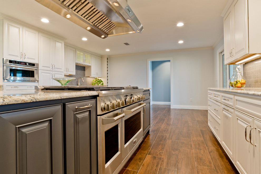 Eat-in kitchen - large transitional galley porcelain tile eat-in kitchen idea in Miami with an undermount sink, raised-panel cabinets, white cabinets, granite countertops, gray backsplash, porcelain backsplash, stainless steel appliances and an island