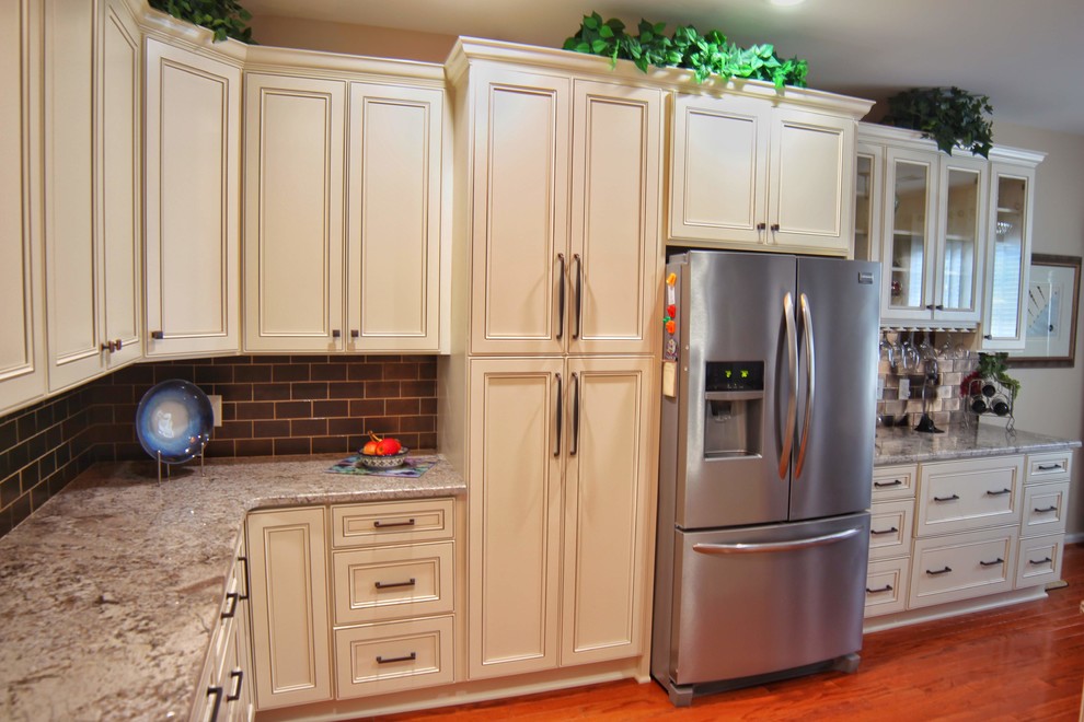 Inspiration for a mid-sized u-shaped medium tone wood floor and brown floor kitchen remodel in Charleston with an undermount sink, raised-panel cabinets, beige cabinets, granite countertops, brown backsplash, ceramic backsplash, stainless steel appliances and beige countertops