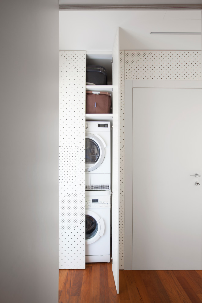 Photo of a small contemporary single-wall utility room in Milan with a drop-in sink, beaded inset cabinets, white walls, dark hardwood floors and a stacked washer and dryer.