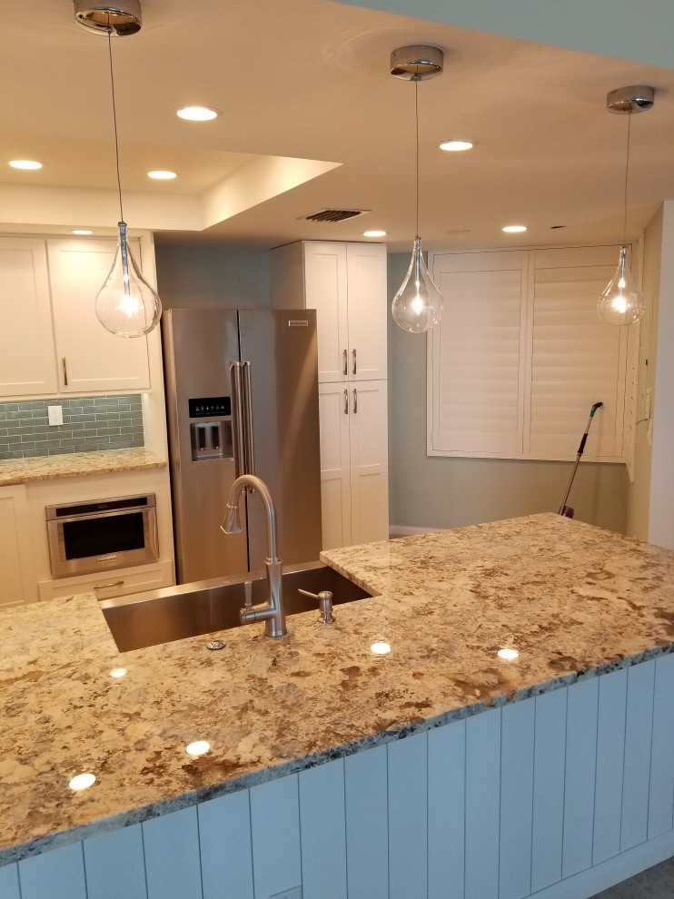 Inspiration for a small beach style galley separate kitchen in Tampa with a farmhouse sink, raised-panel cabinets, white cabinets, granite benchtops, blue splashback, glass tile splashback, stainless steel appliances, ceramic floors, a peninsula, brown floor and brown benchtop.