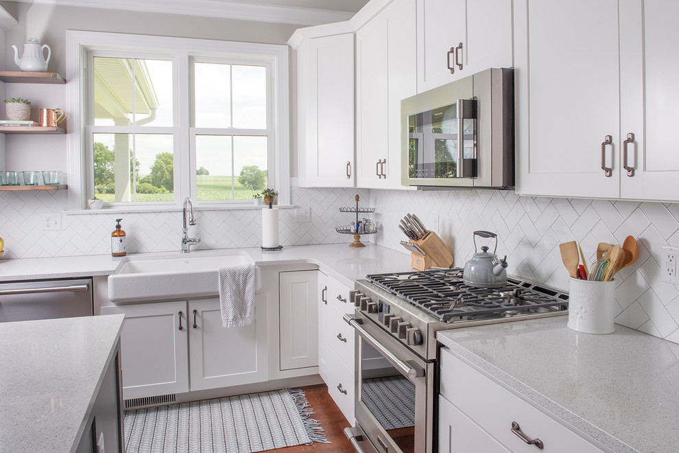 This is an example of a mid-sized transitional l-shaped open plan kitchen in Other with a farmhouse sink, shaker cabinets, white cabinets, white splashback, panelled appliances, medium hardwood floors, with island, brown floor, quartzite benchtops and subway tile splashback.