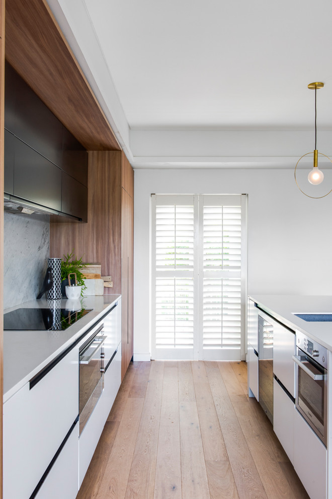 Mid-sized contemporary galley kitchen pantry in Sydney with an undermount sink, light wood cabinets, solid surface benchtops, white splashback, marble splashback, stainless steel appliances, light hardwood floors and with island.