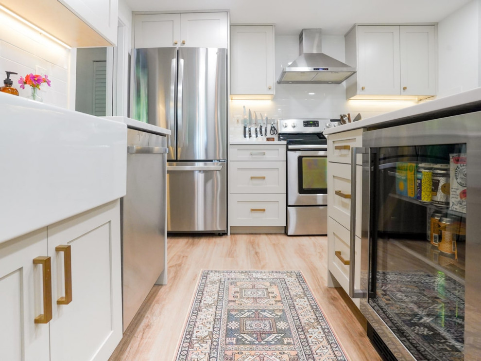 Photo of a mid-sized contemporary galley eat-in kitchen in Seattle with a farmhouse sink, shaker cabinets, white cabinets, quartz benchtops, white splashback, subway tile splashback, stainless steel appliances, vinyl floors, with island, brown floor, white benchtop and timber.