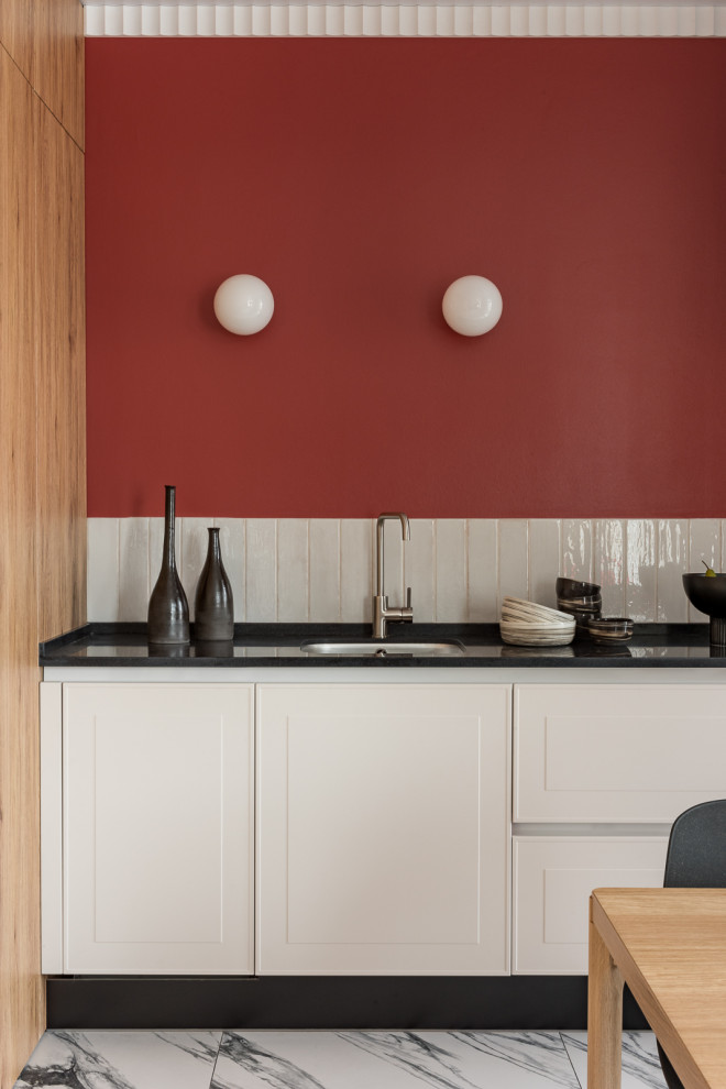 Пример оригинального дизайна: угловая кухня среднего размера в стиле модернизм с обеденным столом, врезной мойкой, белыми фасадами, белым фартуком, фартуком из керамической плитки, полом из керамогранита, белым полом, черной столешницей и акцентной стеной