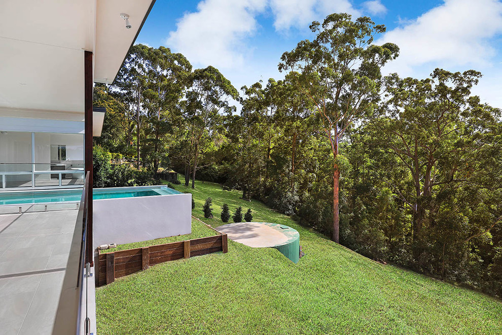 Large modern backyard rectangular infinity pool in Sunshine Coast with tile.