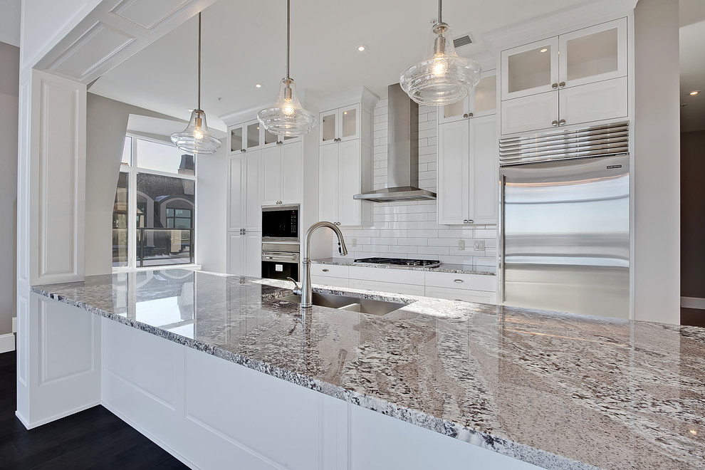 Large traditional galley separate kitchen in Calgary with an undermount sink, recessed-panel cabinets, white cabinets, quartz benchtops, white splashback, subway tile splashback, stainless steel appliances, dark hardwood floors, a peninsula and brown floor.