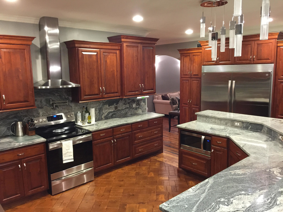 Photo of a large traditional u-shaped kitchen in Minneapolis with raised-panel cabinets, medium wood cabinets, grey splashback, stainless steel appliances, with island and brown floor.