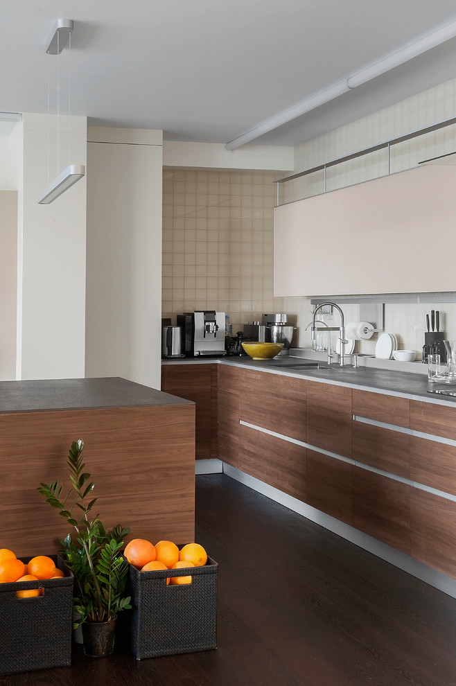This is an example of a mid-sized contemporary galley open plan kitchen in Moscow with an integrated sink, flat-panel cabinets, medium wood cabinets, solid surface benchtops, white splashback, ceramic splashback, stainless steel appliances, dark hardwood floors, with island, brown floor and grey benchtop.