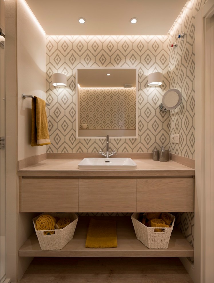 This is an example of a mid-sized contemporary 3/4 bathroom in Bilbao with flat-panel cabinets, light wood cabinets, beige tile, ceramic tile, laminate floors, a drop-in sink, wood benchtops, brown floor, multi-coloured walls and beige benchtops.