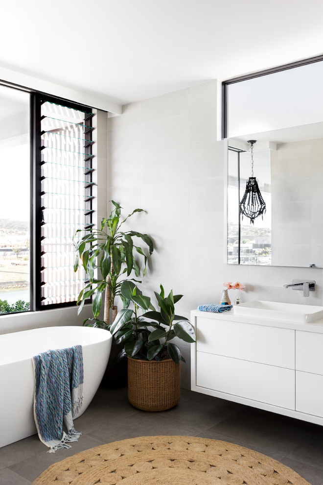 Photo of a contemporary master bathroom in Melbourne with flat-panel cabinets, white cabinets, a freestanding tub, gray tile, grey walls, a drop-in sink, grey floor, white benchtops, porcelain tile, porcelain floors and engineered quartz benchtops.