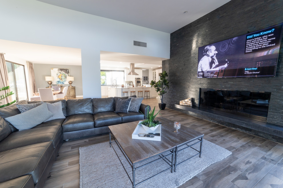 Imagen de sala de estar abierta minimalista grande con marco de chimenea de piedra y televisor colgado en la pared