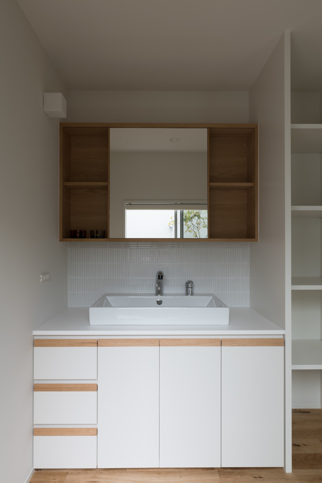 This is an example of a modern powder room in Other with flat-panel cabinets, white cabinets, white tile, matchstick tile, white walls, a vessel sink and beige floor.