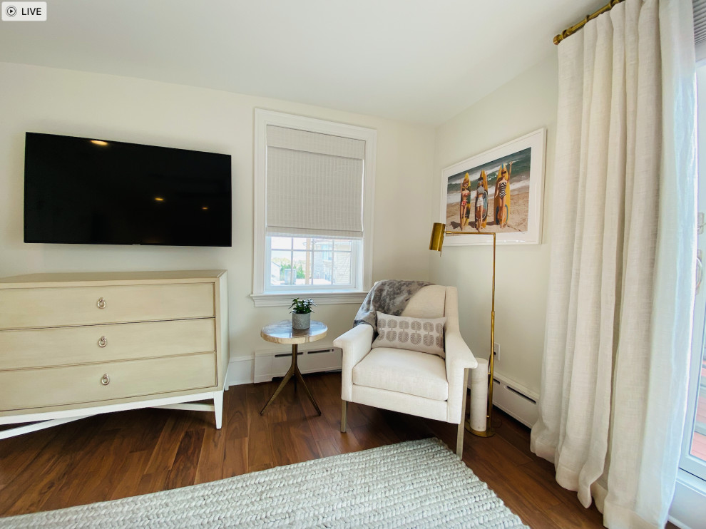 Modelo de habitación de invitados costera grande con paredes blancas, suelo de madera oscura, suelo marrón y papel pintado