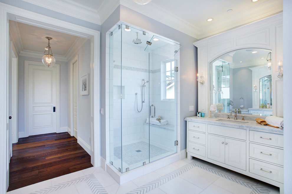 Inspiration for a traditional bathroom in Los Angeles with an undermount sink, raised-panel cabinets, white cabinets, a corner shower, white tile and grey walls.
