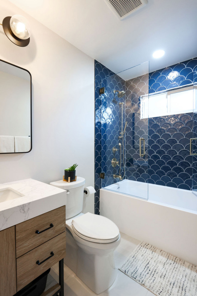 Photo of a mid-sized contemporary kids bathroom in San Diego with flat-panel cabinets, brown cabinets, an alcove tub, a shower/bathtub combo, a two-piece toilet, blue tile, porcelain tile, white walls, porcelain floors, an undermount sink, engineered quartz benchtops, grey floor, a hinged shower door, multi-coloured benchtops, a niche, a single vanity and a freestanding vanity.