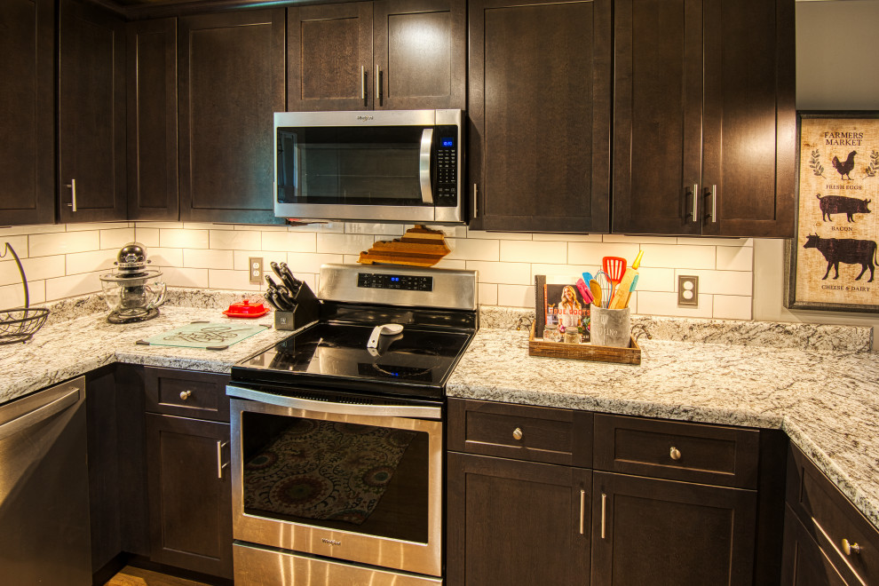 Example of a mid-sized transitional u-shaped light wood floor and brown floor open concept kitchen design with a drop-in sink, shaker cabinets, gray cabinets, laminate countertops, white backsplash, subway tile backsplash, stainless steel appliances, a peninsula and white countertops
