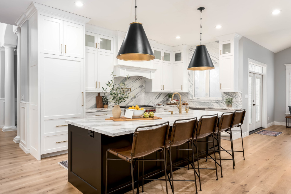Large l-shaped light wood floor and brown floor open concept kitchen photo in Salt Lake City with a farmhouse sink, recessed-panel cabinets, white cabinets, marble countertops, multicolored backsplash, marble backsplash, paneled appliances, an island and multicolored countertops