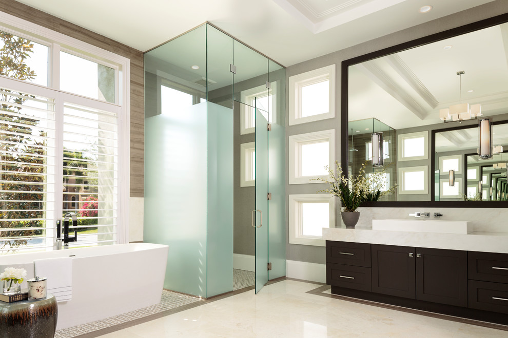 Inspiration for an expansive contemporary master bathroom in Miami with shaker cabinets, dark wood cabinets, a freestanding tub, a curbless shower, a one-piece toilet, brown tile, white tile, porcelain tile, grey walls, marble floors, a vessel sink, quartzite benchtops, white floor and a hinged shower door.
