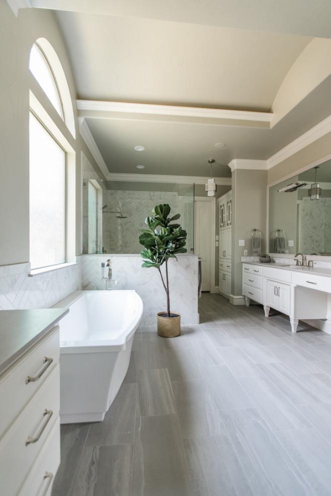 This is an example of a large transitional master bathroom in Dallas with raised-panel cabinets, white cabinets, a freestanding tub, a corner shower, a two-piece toilet, gray tile, porcelain tile, green walls, porcelain floors, an undermount sink, marble benchtops, brown floor, an open shower, white benchtops, a niche, a double vanity, a built-in vanity and vaulted.